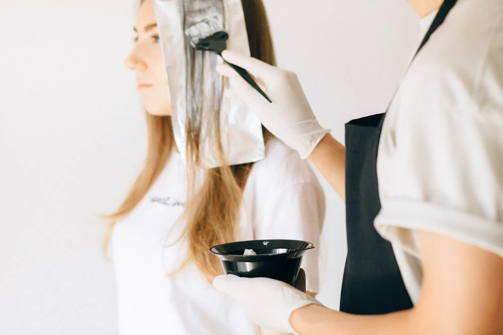 Estilista aplica tinte con brocha sobre papel aluminio en el cabello de una clienta